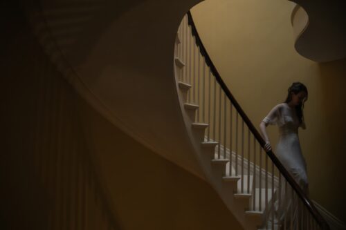 A moody photograph of a bride descending the stairs at her Back Bay brownstone with yellow walls, photographed by Spagnolo Photography as part of her micro-wedding photography package.