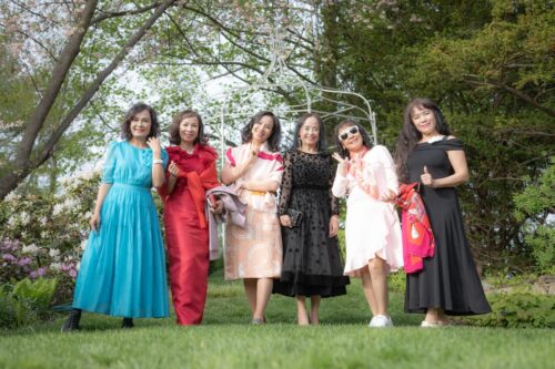 Guests in colorful dresses smile at the camera in the garden of Long Hill Estate during a charming micro-wedding.