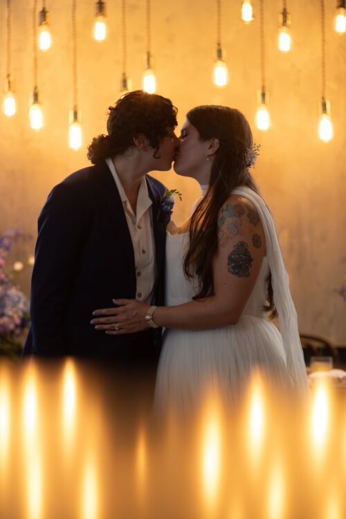 An LGBTQ couple kiss while framed by yellow light at their micro-wedding at the Ledger restaurant in Salem, MA, photographed in a creative, artistic style by Spagnolo Photography as part of their micro-wedding package with two photographers.