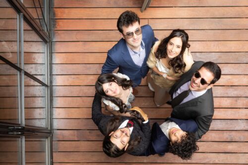 A bride and her guests stand in a circle arms around one another as they look up at the camera during a micro-wedding photographed creatively by Spagnolo Photography as part of their artistic photography package.